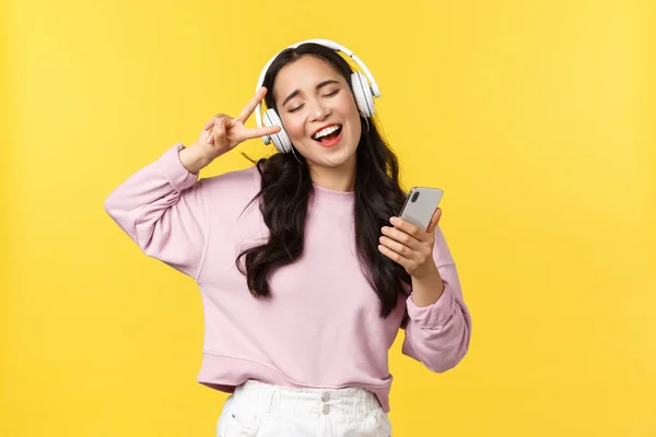 Gente emociones, estilo de vida ocio y concepto de belleza. Despreocupado mujer asiática guapa cerrar los ojos y bailar relajado con el teléfono inteligente, escuchar música en los auriculares, cantar karaoke — Foto de Stock