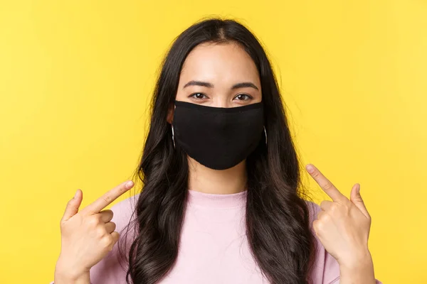 Covid-19, estilo de vida social-distanciamiento, prevenir el concepto de propagación del virus. Chica alegre asiática, sonriendo y apuntando a la mascarilla, recomiendan usar medidas de protección durante la pandemia de coronavirus — Foto de Stock