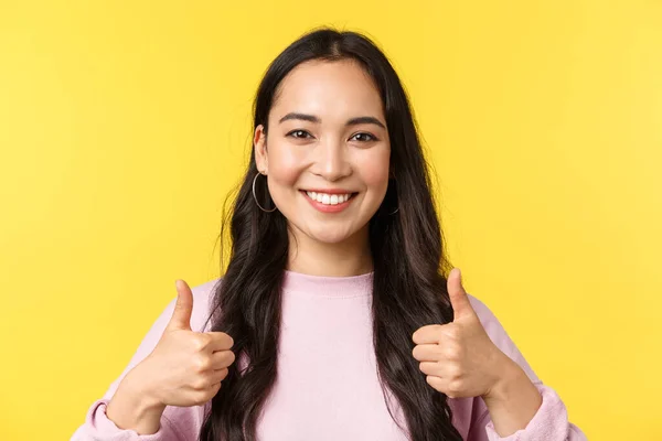 Människor känslor, livsstil fritid och skönhet koncept. Upbeat leende asiatisk flicka visar tummen upp i godkännande, stående gul bakgrund, överens och stöd idé, gul bakgrund — Stockfoto