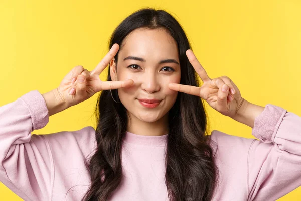 Az emberek érzelmei, életmód szabadidő és szépség koncepció. Közelkép optimista kawaii ázsiai lány, amely békejeleket a szemek felett, és mosolygós, mutatnak pozitív boldog kifejezés, sárga háttér — Stock Fotó