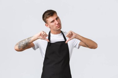 Çalışanlar, bakkallar ve kahve dükkanı konsepti. Havalı ve kendine güvenen ciddi barista, siyah önlüklü garson kararlı bir ifadeyle kendini gösteriyor, konuklarla ilgileniyor, beyaz arka planda.