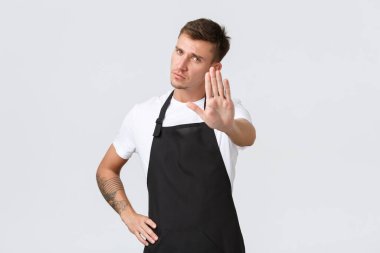 Çalışanlar, bakkallar ve kahve dükkanı konsepti. Ciddi görünümlü hoşnutsuz barista, siyah önlüklü garson dur işareti için elini uzat, kafeye girmeni yasakla, eylemi yasakla, beyaz arka plan