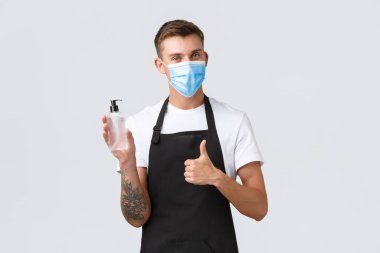 Coronavirus, kafelerde ve restoranlarda sosyal mesafeler, pandemik konsept sırasında iş. Markette, kahvecide ya da garsonda çalışan neşeli bir satıcı. Dezenfekte için baş parmak ve el dezenfektanı.