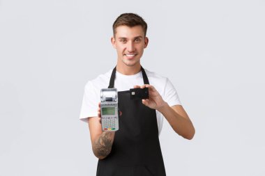 Perakende işi, kafe ve restoran, çalışanlar konsepti. Yakışıklı, güler yüzlü garson. Ulaşılmaz ödeme yolu gösteriyor. POS terminali ve kredi kartını tutuyor.