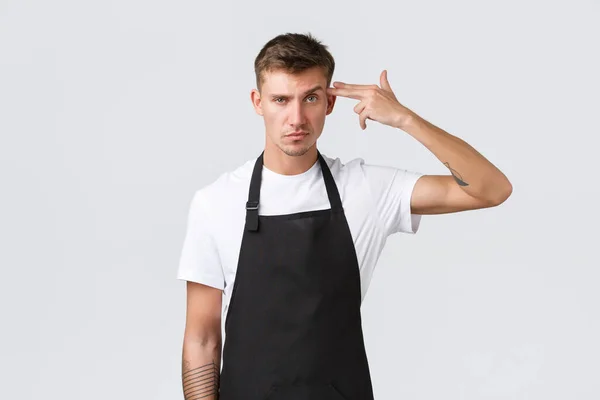 Employees, grocery stores and coffee shop concept. Bothered and distressed barista making fake gun sign over head and grimacing pissed-off, shooting himself tired, white background — Stock fotografie