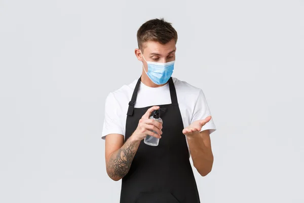 Coronavirus, social distancing in cafes and restaurants, business during pandemic concept. Barista, store employee disinfecting hands with hand sanitizer, waiter working in medical mask — Stock Photo, Image
