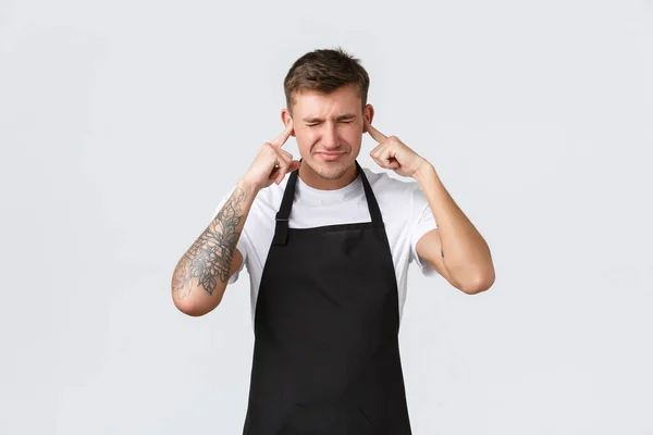 Employees, grocery stores and coffee shop concept. Bothered and annoyed barista, waiter in cafe hate loud music, awful taste of manager, shut ears and grimacing from dislike, white background — Stock Photo, Image
