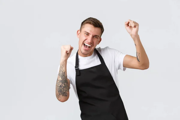 Empregados, mercearias e conceito de café. Garçom carismático amigável feliz sorrindo, dançando alegremente, apreciando a abertura do café após o bloqueio covid-19, levantando as mãos para cima e dizer sim — Fotografia de Stock