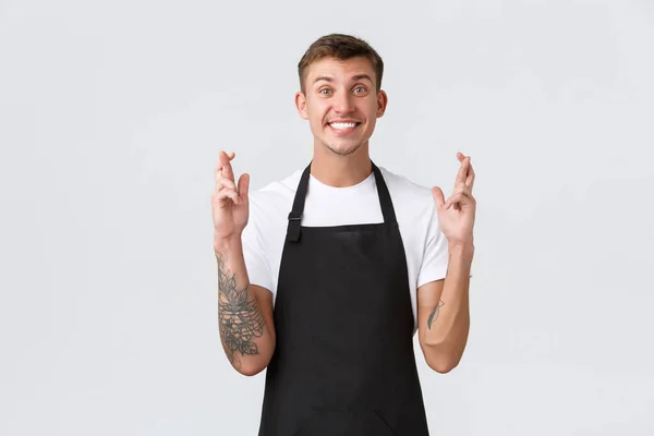 Employees, grocery stores and coffee shop concept. Hopeful excited smiling barista, handsome waiter or grocery store worker cross fingers good luck, making wish over white background — Stock Photo, Image
