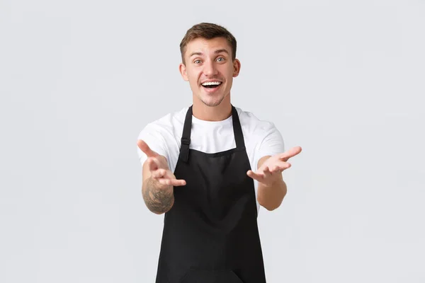 Small business owners, coffee shop and staff concept. Friendly happy smiling barista, cafe entrepreneur in black apron glad see guests after covid-19 closing, reaching hands forward with rejoice — Stock Photo, Image