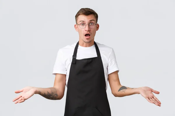 Kleine winkeliers, café en restaurant medewerkers concept. Geschokt en verward barista, ober in zwart schort handen omhoog verbaasd, open mond clueless, witte achtergrond — Stockfoto