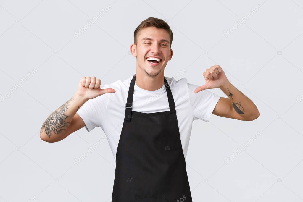 Small business owners, cafe shop and staff concept. Handsome happy barista in black apron guarantee perfect service during his shift, pointing himself and laughing joyful, make best coffee in town