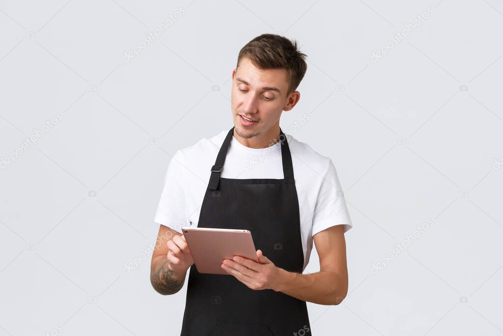 Small business, coffee shop and cafe employees concept. Handsome young guy barista, waiter taking order, serving tables in restaurant, writing order in digital tablet, white background
