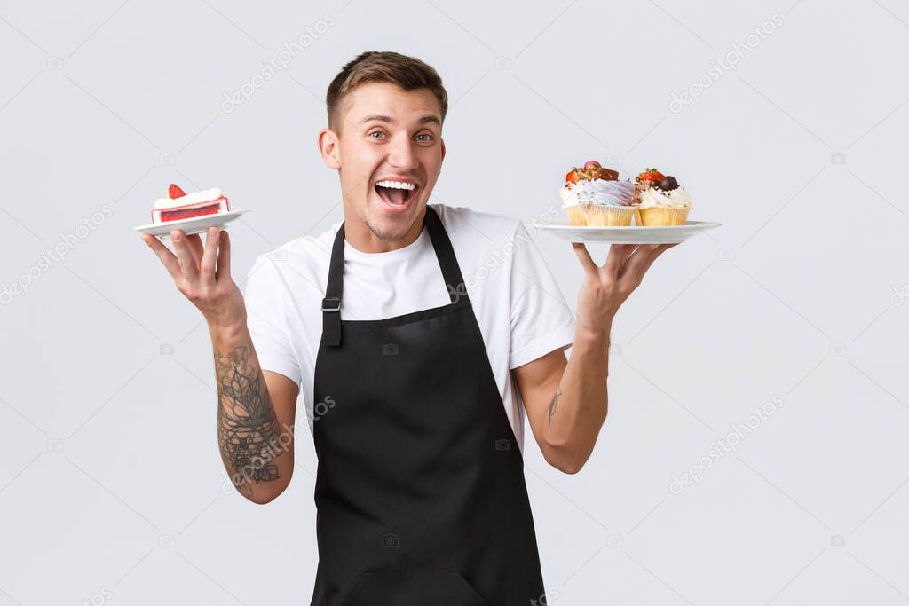 Small retail business, coffee shops and bakery concept. Enthusiastic handsome barista, waiter holding cupcakes and cake, selling desserts to clients, smiling upbeat over white background