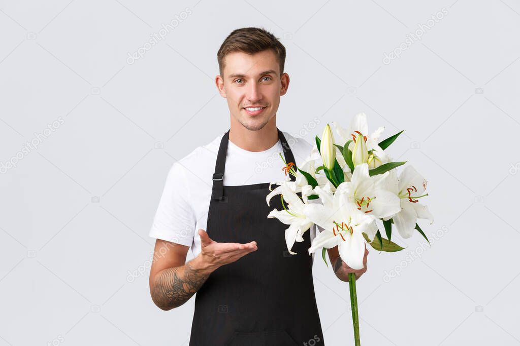 Small business, retail and employees concept. Handsome salesman in black apron, made beautiful flowers, florist in store selling lilies, smiling friendly at customer, white background