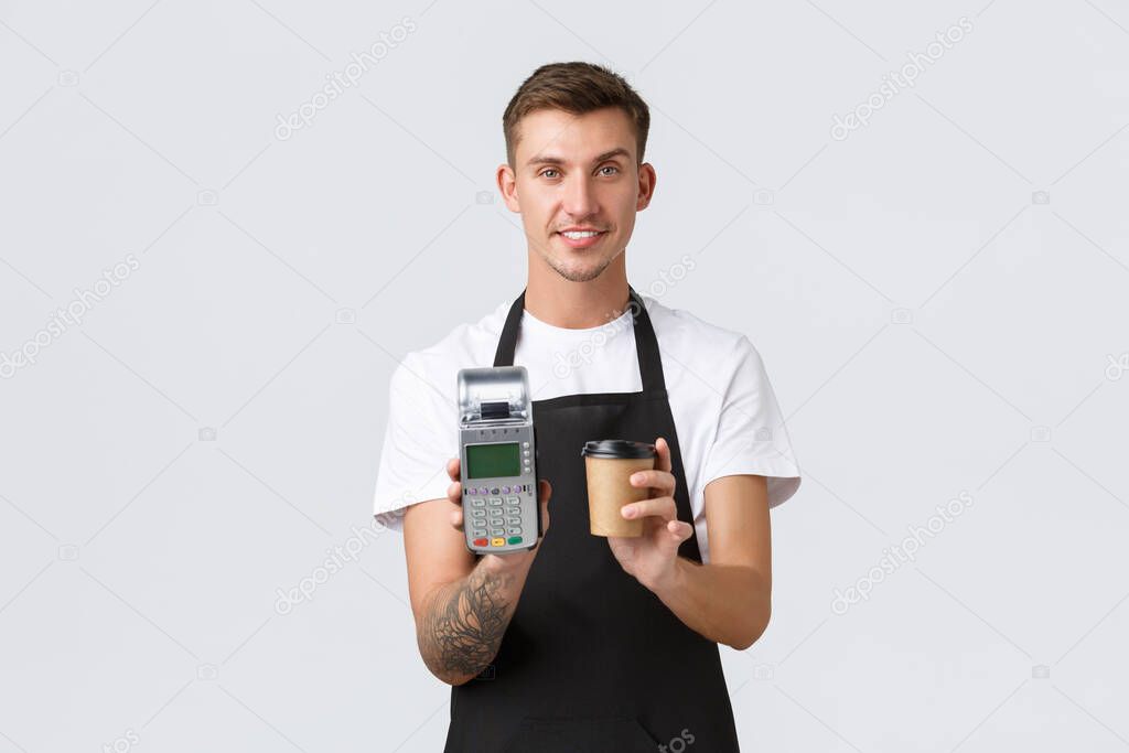 Small business owners, coffee shop and staff concept. Handsome smiling barista, waiter serving takeaway drink in cafe, giving client cup and payment terminal, white background