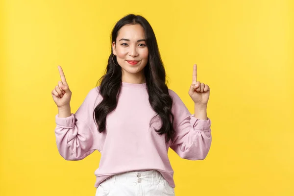 As pessoas emoções, estilo de vida e conceito de moda. Agradável sorrindo mulher atraente em roupas elegantes apontando os dedos para cima, demonstrar link do produto, publicidade sobre fundo amarelo — Fotografia de Stock