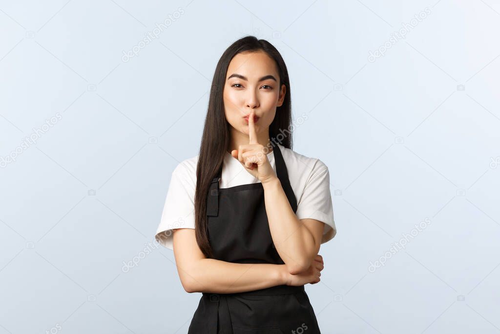 Coffee shop, small business and startup concept. Sassy good-looking asian female barista prepared secret, hush with finger pressed to lips, looking sensual and mysterious, be quiet