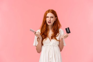 Sinirli ve sinirli kızıl saçlı bir kız, garip online bankacılık sisteminden memnun değil, siparişini alamıyor, elinde akıllı telefon ve kredi kartı ile rahatsız oluyor.