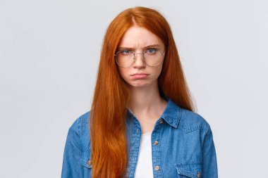 Yakın plan portre katı ve kızgın, kızgın, kasvetli, kızgın kızıl saçlı kız gücenmiş ve hayal kırıklığına uğramış, somurtkan, öfkeli, bir şeyleri kınayan, kuşkucu ve rahatsız beyaz arka plan