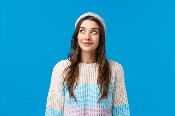 Menina curiosa sobre o que acontece no canto, espreitando e sorrindo animado, quer ver algo interessante acontecendo, de pé fundo azul otimista com lindo sorriso, use camisola de inverno e chapéu — Fotografia de Stock