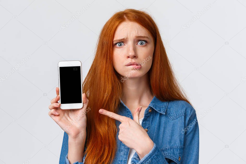 Worried, insecure and alarmed cute redhead girl asking for advice having problems messaging with stranger on dating app, dont know what answer standing nervous pointing finger at smartphone display
