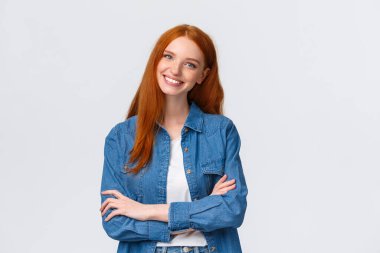 Profesyonellik, takım çalışması konsepti. Belden yukarı vuruşlar, hoş kızıl saçlı genç, üniversite öğrencisi, kot gömlekli kızıl kız, göğüslerinin üzerinde çapraz eller, mutlu bir gülümseme, kendine güvenini ifade et.