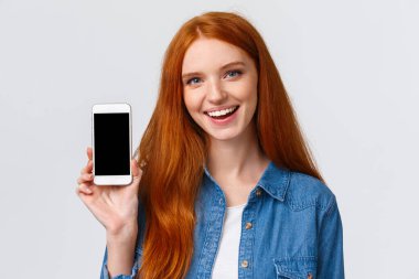 Modern çağın portresi mavi gözlü, sevimli, kızıl saçlı kadın akıllı telefon ekranını ve gülümsemesini gösteren yeni bir uygulama edinin, reklam oyunu veya fotoğraf filtresi uygulaması