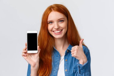 Uygulama kullanarak tatmin olmuş güzel kızıl saçlı bir kadının yakın plan portresi, indirmeyi tavsiye edin, fotoğraf uygulaması, internet mağazası, akıllı telefon görüntüsü ve başparmak kaldırma gibi