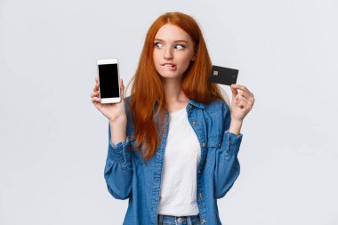Kız, süper indirimli bir şey almayı düşünüyor. Geçici ve hayalperest kızıl saçlı kadın akıllı telefona bakıyor, mobil alışveriş uygulamasına bakıyor, kredi kartını tutuyor, dudağını ısırmaya hevesli.