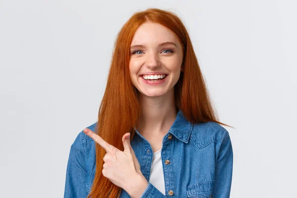 Close-up portret uitgaande goed uitziende vrolijke roodharige tiener meisje in casual outfit, lachen en praten, bespreken recente gebeurtenis, wijzende vinger naar links banner, raden reclame — Stockfoto