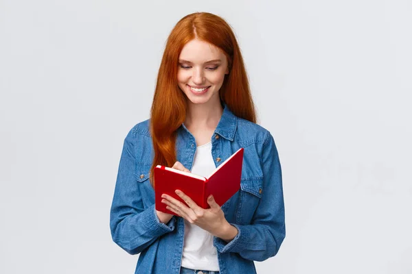 Creative and talented good-looking female college student prepare schedule for tomorrow classes, writing in diary, taking notes in fancy notebook, standing white background