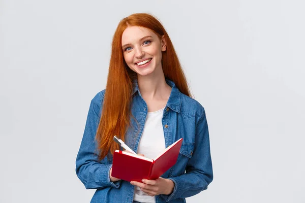 Karismatisk begåvad söt rödhårig kvinnlig student studerar, anteckna efter lärare i anteckningsbok, skriva i dagbok, rita klotter stående vit bakgrund glad — Stockfoto