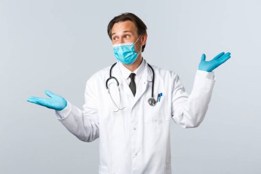 Covid-19, virüsü önleme, sağlık çalışanları ve aşı konsepti. Tıbbi maskeli ve eldivenli karizmatik doktor, yan tarafları gösteriyor, iki ürün gösteriyor, şaşırmış görünüyor