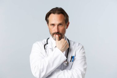 Covid-19, virüsü önleme, sağlık çalışanları ve aşı konsepti. Endişeli, ciddi görünümlü, beyaz önlüklü, ısıran, odaklanmış ve hasta semptomlarını dinleyen doktorların yakın çekimi.