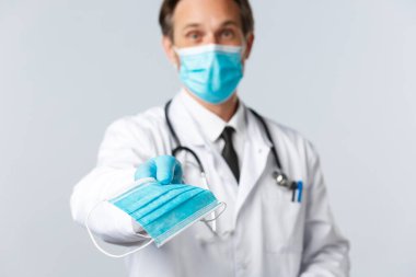 Covid-19, virüsü önleme, sağlık çalışanları ve aşı konsepti. Dost canlısı doktor, Coronavirus salgını sırasında sağlıklı kalabilmek için hasta maskesi takıyor. Doktor PPE 'yi veriyor.
