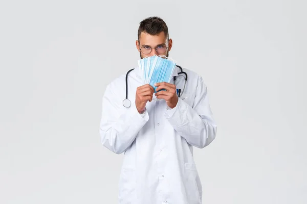 Εργάτες υγείας, ιατρική ασφάλιση, πανδημία και covid-19 έννοια. Αστείος όμορφος γιατρός, ισπανόφωνος γιατρός με λευκό παλτό και γυαλιά, που δείχνει ιατρικές μάσκες, να το χρησιμοποιήσετε κατά τη διάρκεια του κορωναϊού. — Φωτογραφία Αρχείου