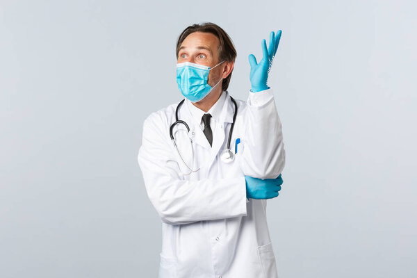 Ковид-19, профилактика вируса, медицинские работники и концепция вакцинации. Возбужденный оптимистичный врач в медицинской маске и перчатках, подняв руку вдумчивый, есть идея, выглядеть изумленным

