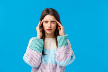 Akşamdan kalma, sağlık ve insan konsepti. Stresli genç bir kadın baş ağrısı çekiyor, gözleri kapalı tapınaklara dokunuyor, ilaçla kolay bir acı çekmeye çalışıyor, migren ağrısı çekiyor, mavi arka planda duruyor.