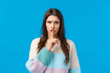 Kızgın ve sinirli, sinirli otoriter kız kameraya şşşş yapıyor, kızgın kameraya bakıyor sessiz olun, susun, herkesin sessiz olmasını, mavi arka planda durmasını istiyor.