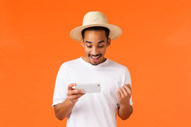 Zafer kazanan mutlu, Afro-Amerikan adam yarışı kazanıyor, zor seviye oyunu geçiyor, yumruk pompası evet diyor ve gülümsüyor, akıllı telefonu yatay olarak tutuyor, turuncu arka plan