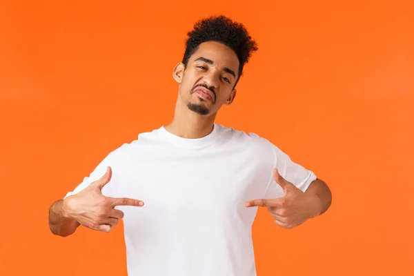 Sassy et confiant homme afro-américain affirmatif, agissant cool et insolent, se montrant fier, vantard debout fond orange, show-off, faire impression, porter un t-shirt blanc — Photo