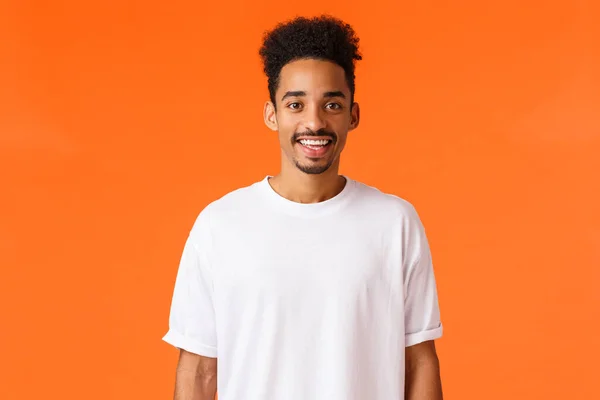 Χαρούμενος νεαρός hipster αφροαμερικανός με μουστάκι και αφρο κούρεμα, φορώντας λευκό t-shirt, χαμογελώντας χαριτωμένο αναζητούν κάμερα ευτυχισμένη, στέκεται πορτοκαλί φόντο εκφράζουν θετικότητα — Φωτογραφία Αρχείου