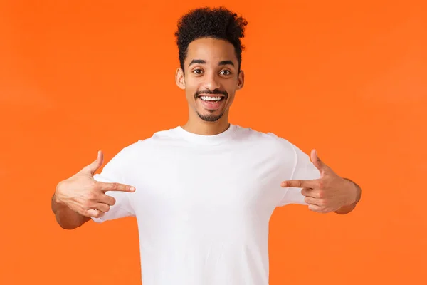 Otimista feliz e bonito afro-americano hipster cara, quer fazer uma mudança, voluntário, disposto a participar, apontando-se dizendo que ele é um, candidato perfeito, de pé fundo laranja — Fotografia de Stock