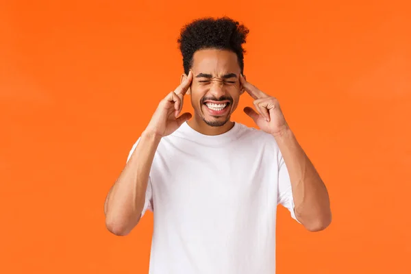 Homem afro-americano angustiado e tenso em t-shirt branca, dentes apertados, olhos fechados e têmporas de toque, sensação de enxaqueca ou dor de cabeça, tentando acalmar e pensar em linha reta, fundo laranja — Fotografia de Stock