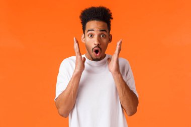 Etkilenmiş, afro-amerikan adam müthiş bir şey gördü, şaşırdı ve eğlendi, indirimleri kontrol etti, sezon indirimleri, çarpıcı performanslara katıldı, turuncu arka planda durdu.