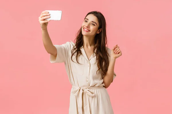 Skönhet, mode och kvinnor koncept. Tillåta ung feminin kvinna som tar selfie i ny klänning, posta nytt foto på nätet, leende anbud och söt kamera, stående rosa bakgrund — Stockfoto