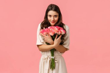 Şefkat, romantizm ve aşk konsepti. Çekici esmer kadın, güzel çiçekler alan kız arkadaş buketi kucaklayan ve gülümseyen kamera keyifli sevgi ve mutluluk gösteren pembe arka plan.