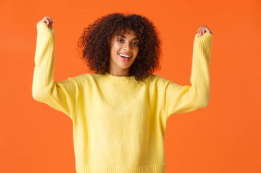 Relish, triumphing and champion concept. Excited happy african-american young girl with afro haircut, raising hands up from excitement and happiness, cheering winning, celebrate victory