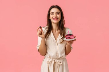 Doğum günü kızı lezzetli pastalar yiyor, mumları üflüyor ve neşeyle gülümsüyor, yabanmersini tutuyor, arkadaşlarıyla doğum gününü kutluyor, pembe arka planda sırıtarak duruyor.